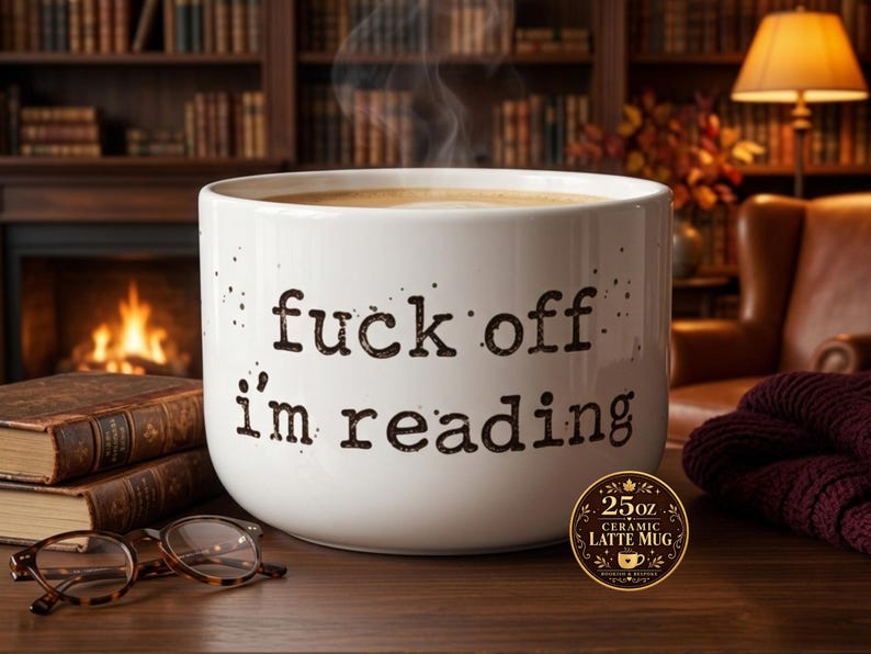 K&ouml;nnte beinhalten: Ein wei&szlig;er 710 ml Keramik-Latte-Becher mit schwarzem Text, der "fuck off i'm reading" in einer Schreibmaschinen-Schriftart zeigt. Der Becher hat eine breite, zylindrische Form und enth&auml;lt ein dampfendes Getr&auml;nk.