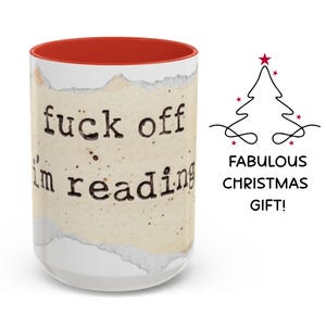 K&ouml;nnte beinhalten: Ein wei&szlig;er Keramikbecher mit rotem Innenraum, verziert mit einer Grafik aus zerrissenem Papier und dem schwarzen Schreibmaschinen-Text "fuck off i'm reading". Rechts daneben befindet sich ein schwarzes Weihnachtsbaum-Symbol &uuml;ber dem Text "FABULOUS CHRISTMAS GIFT!".