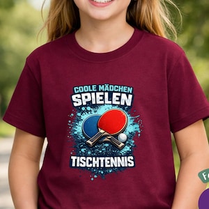 Puede incluir: Una camiseta granate con el texto alem&aacute;n "COOLE M&Auml;DCHEN SPIELEN TISCHTENNIS" y un gr&aacute;fico de paletas de ping pong y una pelota. La camiseta tambi&eacute;n tiene el texto "Cooles Geschenk f&uuml;r Tischtennis-Fans".