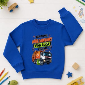 May include: A royal blue long-sleeve sweatshirt featuring a graphic of an orange garbage truck with two trash bins. The text reads "ACHTUNG M&Uuml;LLABFUHR! FINN LUCA KOMMT!" in orange, black, and white lettering above the truck illustration.