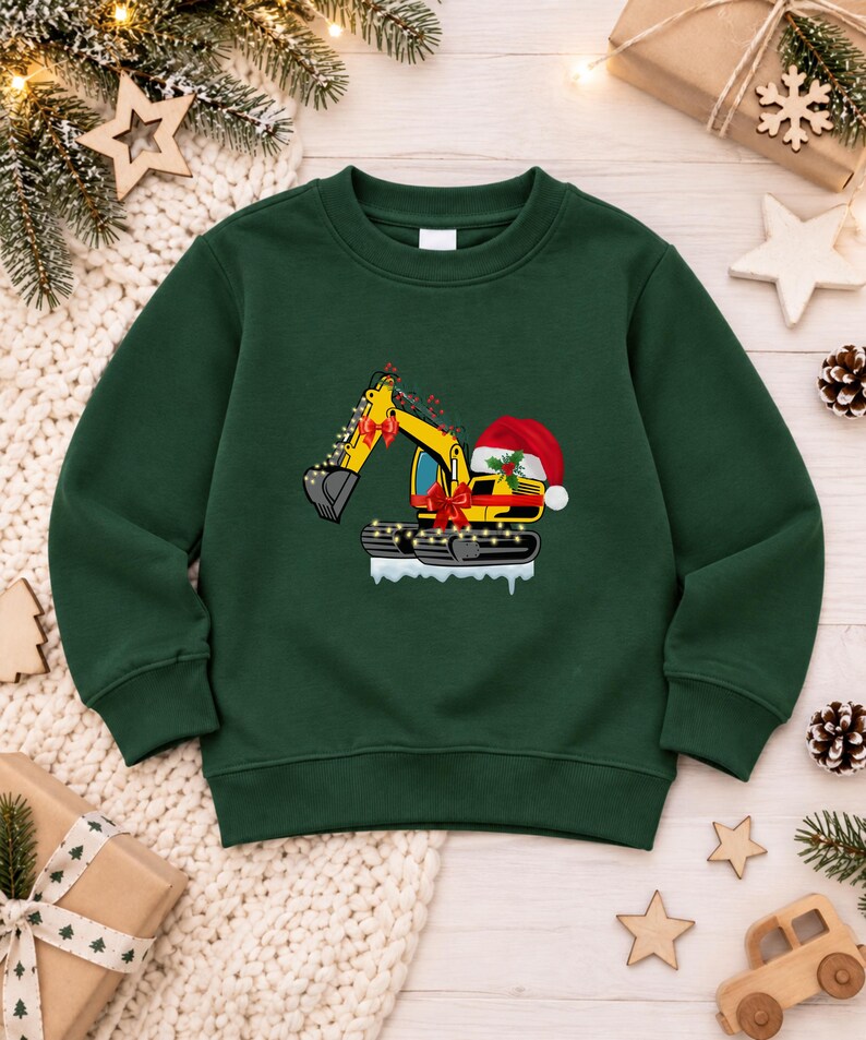 May include: A dark green long-sleeve sweatshirt featuring a graphic of a yellow excavator decorated with Christmas lights, red bows, and a Santa hat. The excavator sits on a patch of white snow, creating a festive holiday-themed design.