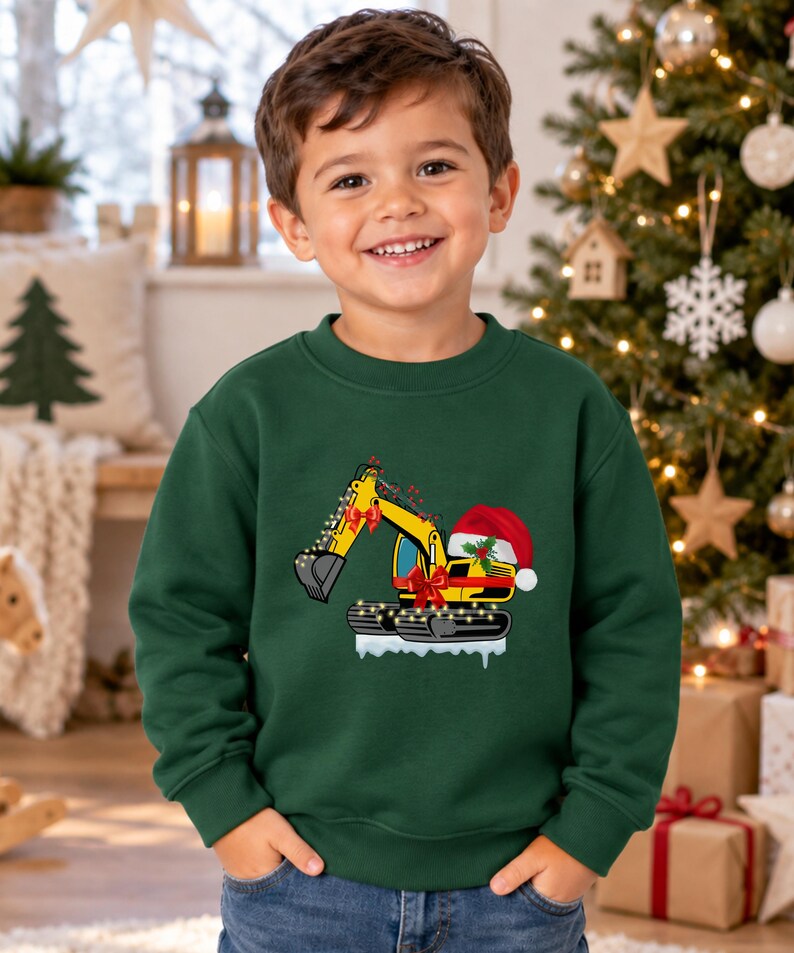 May include: A dark green crewneck sweatshirt featuring a graphic of a yellow excavator decorated with red bows, string lights, and a red Santa hat, positioned on a patch of white snow, worn with blue denim jeans.