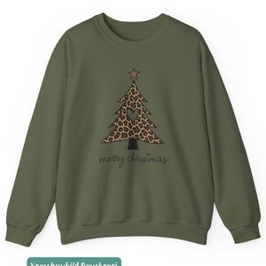 May include: An olive green crewneck sweatshirt featuring a central graphic of a Christmas tree with a brown leopard print pattern, a small star at the top, and a heart-shaped cutout in the center. The text merry christmas is printed below.