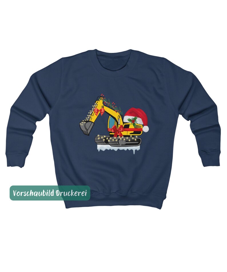 May include: A navy blue long-sleeve sweatshirt featuring a graphic of a yellow excavator decorated with red bows, holly, and string lights. The excavator wears a red Santa hat and sits on a patch of white snow. The text "Vorschaubild Druckerei" is visible.
