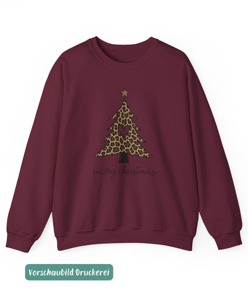 May include: A maroon long-sleeve sweatshirt featuring a central graphic of a Christmas tree with a leopard print pattern, a small brown star at the top, and a dark heart shape in the center. The text merry christmas is printed in black below.