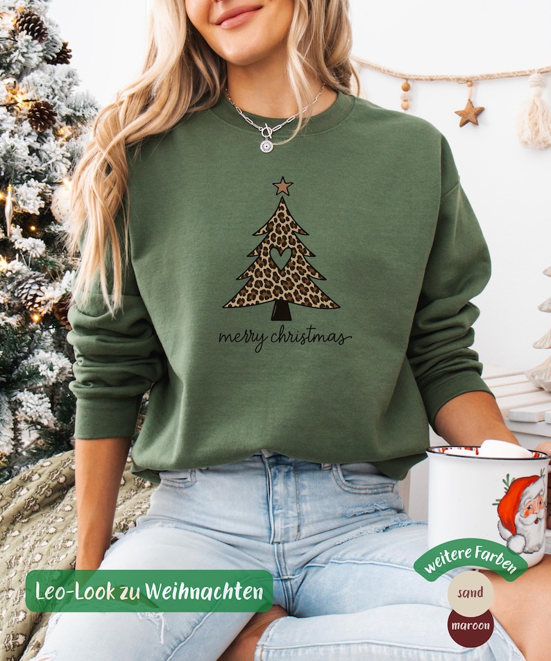 May include: An olive green crewneck sweatshirt featuring a graphic of a Christmas tree with a leopard print pattern, a heart-shaped cutout in the center, and a star on top. The text merry christmas is printed in black cursive below the tree graphic.