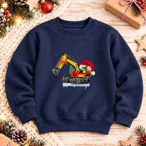 May include: A navy blue crewneck sweatshirt featuring a graphic of a yellow excavator decorated with red bows, a string of lights, and a Santa hat, with the excavator tracks resting on a patch of white snow.