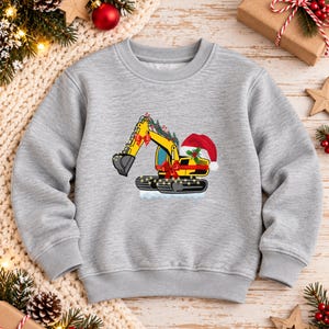 May include: A heather gray crewneck sweatshirt featuring a graphic of a yellow excavator decorated with a red bow, a Santa hat, holly leaves, and string lights. The excavator is positioned on a small patch of white snow, creating a festive scene.
