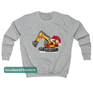 May include: A heather gray crewneck sweatshirt featuring a graphic of a yellow excavator decorated with red bows, a Santa hat, holly berries, and string lights. The excavator sits on a patch of white snow, creating a festive construction theme.
