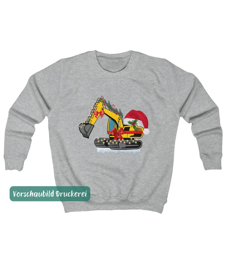 May include: A heather gray crewneck sweatshirt featuring a graphic of a yellow excavator decorated with red bows, a Santa hat, holly berries, and string lights. The excavator sits on a patch of white snow, creating a festive construction theme.