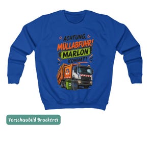 May include: A royal blue long-sleeve sweatshirt featuring a graphic of an orange garbage truck with two trash bins. The text reads ACHTUNG. M&Uuml;LLABFUHR! MARLON KOMMT! in black, orange, and green lettering above the truck illustration.