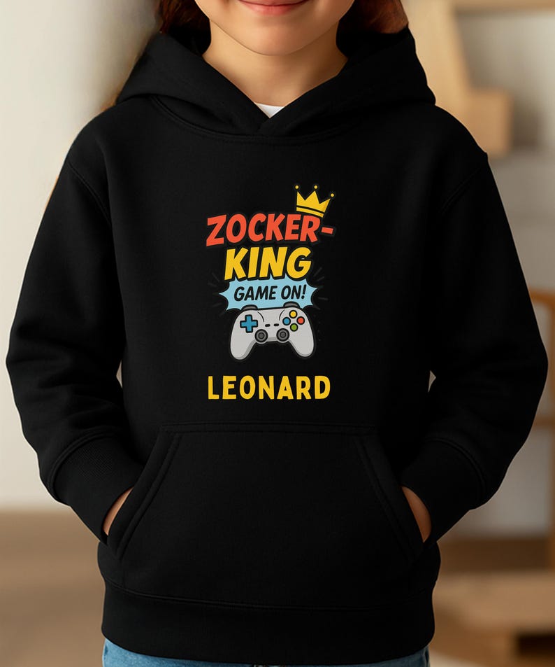 May include: A black hooded sweatshirt featuring a graphic print with the text ZOCKER-KING GAME ON! and LEONARD. The design includes a yellow crown icon above the text and a gray video game controller illustration centered below the text.