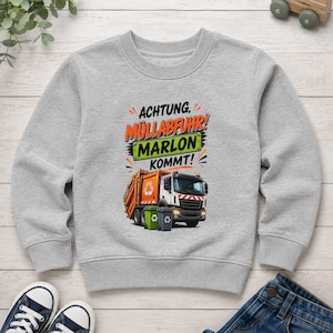 May include: A heather gray long-sleeve sweatshirt featuring a graphic of an orange garbage truck with two recycling bins. The text reads "ACHTUNG, M&Uuml;LLABFUHR! MARLON KOMMT!" with "MARLON" displayed on a green rectangular sign above the truck.