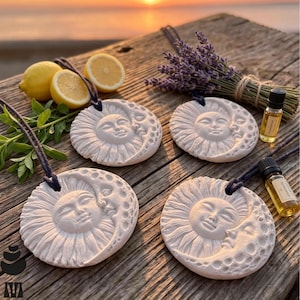 May include: Four circular white ceramic ornaments featuring a relief design of a sun and moon face, each suspended by a dark cord. The set includes two small glass bottles of essential oil, a bundle of dried lavender, and two sliced lemons.