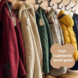 May include: A selection of coats in shades of burgundy, cream, green, and yellow, suspended from black hooks on a wooden wall. Each coat is adorned with a decorative tag. The image includes the text "Coat cupboards smell great."