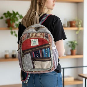 Può includere: Uno zaino colorato con un design patchwork. Lo zaino presenta una varietà di motivi e trame, tra cui strisce, spina di pesce e forme geometriche. Il colore principale è il rosso, con accenti di blu, marrone e beige. Il testo "Himalaya Hemp The Free" è visibile.