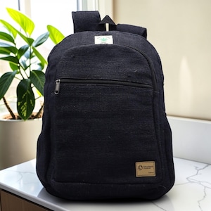 May include: Black backpack with a front zippered pocket and adjustable straps. The backpack has a small tag with a cannabis leaf logo and a larger tag that reads "Student". The bag is made of a textured fabric.