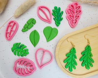 May include: An assortment of leaf-shaped polymer clay cutters in pink and green, alongside matching green leaf earrings with gold-colored hooks. The cutters vary in shape, including a heart, and several leaf designs.