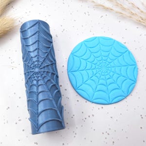 May include: A blue spiderweb-patterned rolling pin and a circular stamp. The rolling pin is cylindrical, and the stamp is round. Both items feature a detailed spiderweb design, ideal for baking or craft projects.