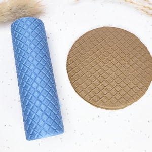 May include: A blue, textured roller and a brown, circular object with a diamond pattern. The roller is cylindrical and stands upright. The circular object is flat and round. Both objects have a repeating diamond pattern.