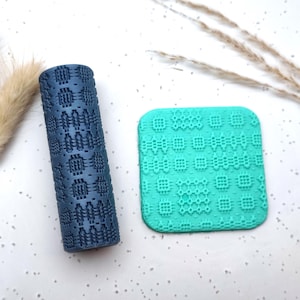 May include: A dark blue patterned rolling pin and a square, turquoise textured stamp. The rolling pin is cylindrical and features a repeating geometric design. The stamp has a similar pattern. Decorative elements are visible in the background.