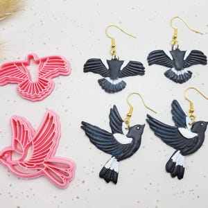 May include: Pink bird-shaped cookie cutters and black, white, and gold bird earrings. The earrings feature a magpie design with gold-coloured hooks. The cookie cutters are labelled #1 and #2.