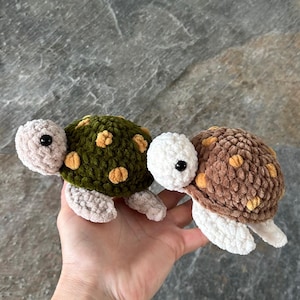 May include: Two small plush turtle toys made of soft, textured yarn. One turtle features a dark green shell with yellow spots and a light beige head and flippers. The other turtle has a brown shell with yellow spots and a white head and flippers.