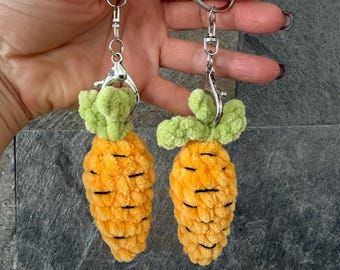 May include: Two orange carrot-shaped keychains with green tops and black details. The keychains are made of a soft, textured material and are attached to silver key rings.