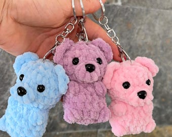 May include: Three plush bear keychains in light blue, lavender, and light pink, each crafted from soft, fuzzy yarn with black plastic bead eyes and noses. The bears are attached to silver-toned metal key rings with lobster claw clasps.