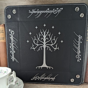 May include: Black leather dice tray with a white tree design and the inscription "One Ring to rule them all" in Elvish script.