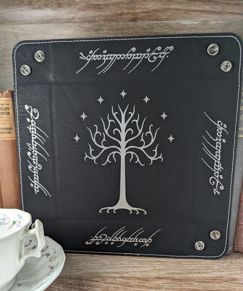 May include: Black leather dice tray with a white tree design and the inscription "One Ring to rule them all" in Elvish script.