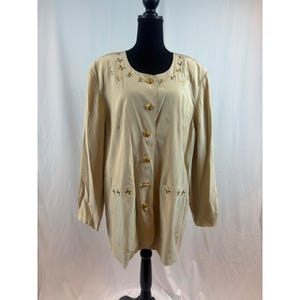May include: A tan-colored button-down jacket with long sleeves. The jacket features gold star embellishments around the neckline and pockets, and gold star-shaped buttons down the front. The jacket is displayed on a black mannequin.