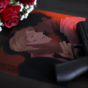 May include: An artistic print depicting two figures in a close embrace, with a black handgun. The artwork is set against a red and black background, with red roses and white flowers in the upper left corner.
