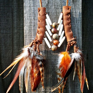 May include: A brown leather necklace with white and brown beads and feathers. The necklace is hanging on a wooden surface.