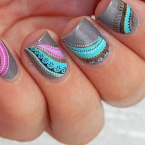May include: Close-up of fingernails with a gray base and colorful geometric designs. The designs feature pink, blue, and white accents.