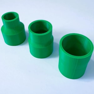 May include: Three green plastic pipe fittings of different sizes. The fittings are cylindrical with a smooth surface.