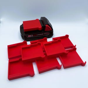 May include: A black and red M18 REDLITHIUM CP 2.0 battery pack with several red battery holders. The battery pack has the text "M18" and "REDLITHIUM CP 2.0" printed on it. The holders are rectangular with a lip on one side.