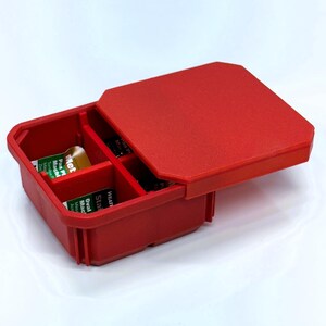 May include: A red plastic storage box with a hinged lid, divided into four compartments. The lid is partially open, revealing the interior. The box contains small items and labels. The box is designed for organizing small parts.
