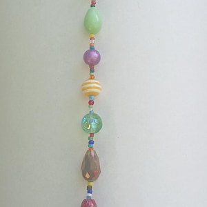 May include: A colorful beaded keychain with a silver peace sign charm. The beads are various shapes and colors, including green, red, blue, and yellow. The keychain is attached to a silver ring.