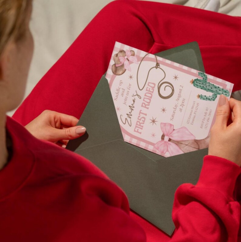 May include: A person holding a First Rodeo invitation in a dark green envelope. The invitation features a pink and white checkered background with a lasso, cactus, and bow illustrations. Text includes "Emma's First Rodeo" and event details.