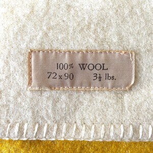 May include: Cream-colored wool blanket with a stitched border and a mustard yellow edge. A rectangular label reads "100% WOOL, 72 x 90, 3 1/2 lbs."