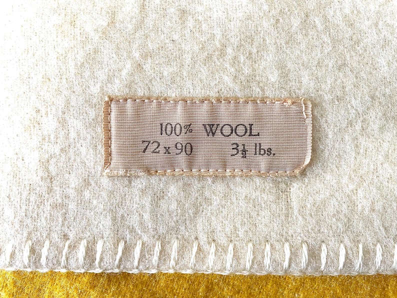 May include: Cream-colored wool blanket with a stitched border and a mustard yellow edge. A rectangular label reads "100% WOOL, 72 x 90, 3 1/2 lbs."