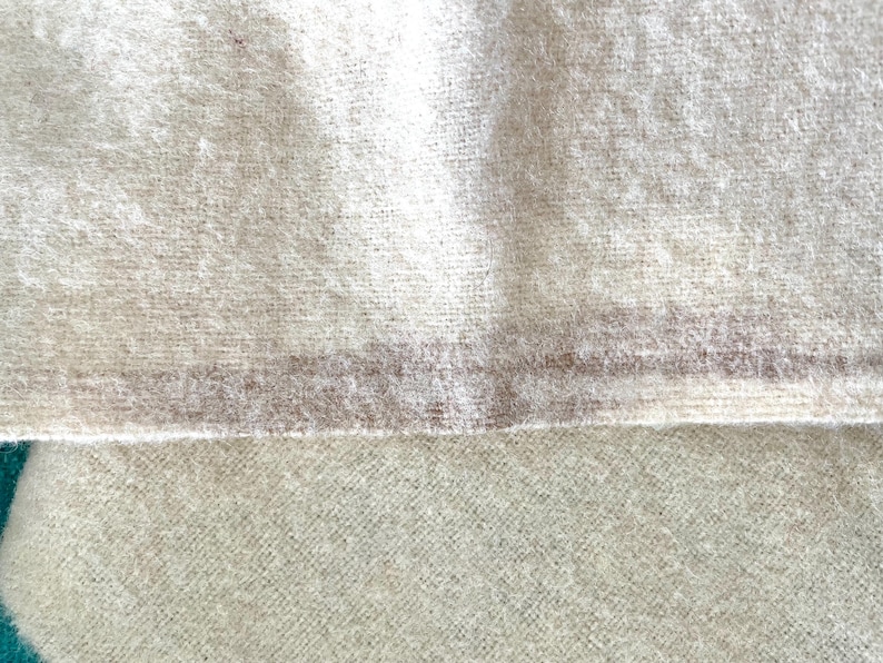 May include: Close-up of a textured, off-white fabric with a subtle, horizontal stripe in a muted brown hue. The fabric appears soft and possibly woven, with a slightly fuzzy texture. The image highlights the material's natural appearance.