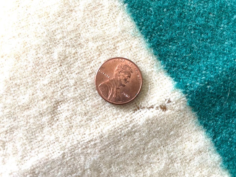May include: A copper penny rests on a textured fabric with white, teal, and off-white stripes. The penny shows the profile of a man and the words "In God We Trust" and the year 2010.
