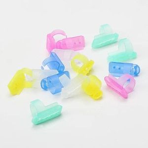 Könnte beinhalten: Eine Sammlung von durchscheinenden Kunststoff-Fingerringen in verschiedenen leuchtenden Farben wie Pink, Blau, Gelb und Grün. Jeder Ring verfügt über eine kleine, flache, rechteckige Plattform am Band, die zum Halten von kleinen Gegenständen oder Kleber dient.