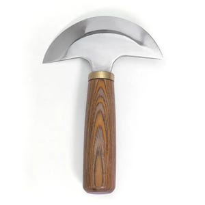 K&ouml;nnte beinhalten: Ein Lederwerkzeugmesser mit einer gebogenen, polierten Stahlklinge und einem Holzgriff. Der Griff ist hellbraun mit einem Holzmaserungsmuster. Ein Messingkragen verbindet Klinge und Griff.