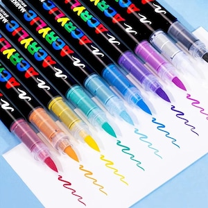 May include: A set of eight acrylic brush markers with black barrels and white text reading ACRYLIC MARKER. Each marker features a clear cap and a coloured brush tip, with corresponding wavy ink lines drawn on white paper in shades of pink, orange, yellow, teal, blue, purple, and black.