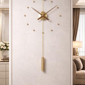 Könnte beinhalten: Moderne Wanduhr mit goldener Oberfläche. Die Uhr hat ein kreisförmiges Zifferblatt mit braunen Zeigern und goldenen Punktmarkierungen. Ein goldfarbenes Pendel hängt unter dem Zifferblatt.