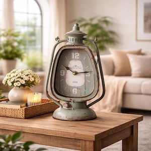 May include: A vintage-style, teal metal clock shaped like a lantern. The clock face has Roman numerals and the text "Champagne de Paris 1891." The clock sits on a wooden table, with a candle and flowers in the background.