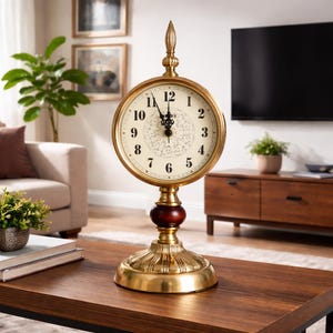 May include: A decorative gold-colored table clock with a cream-colored face and black Roman numerals. The clock has a detailed design and a dark red wooden accent. The clock is on a dark brown wooden table.